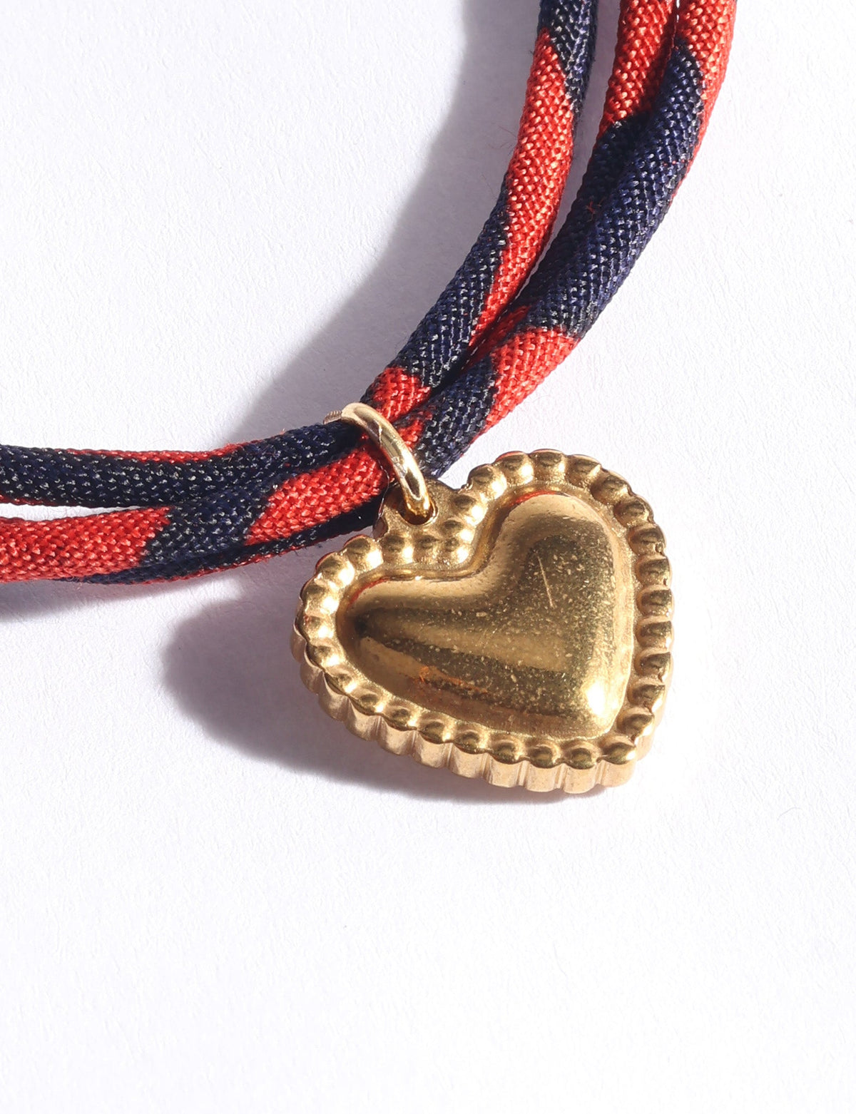 Red and navy twisted cord bracelet with a gold-tone heart-shaped charm, close-up view on white background