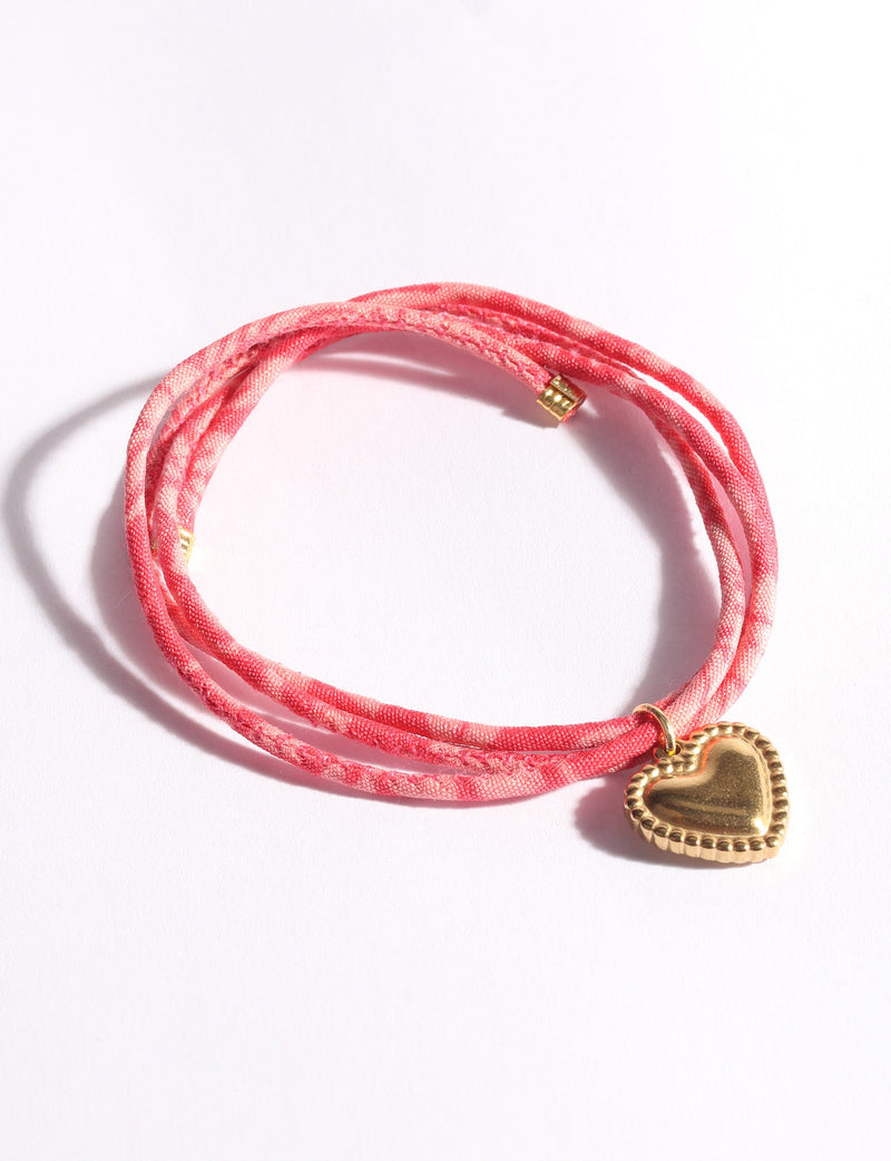 Pink abstract patterned cord bracelet with a gold-tone heart charm, shown coiled on a white background