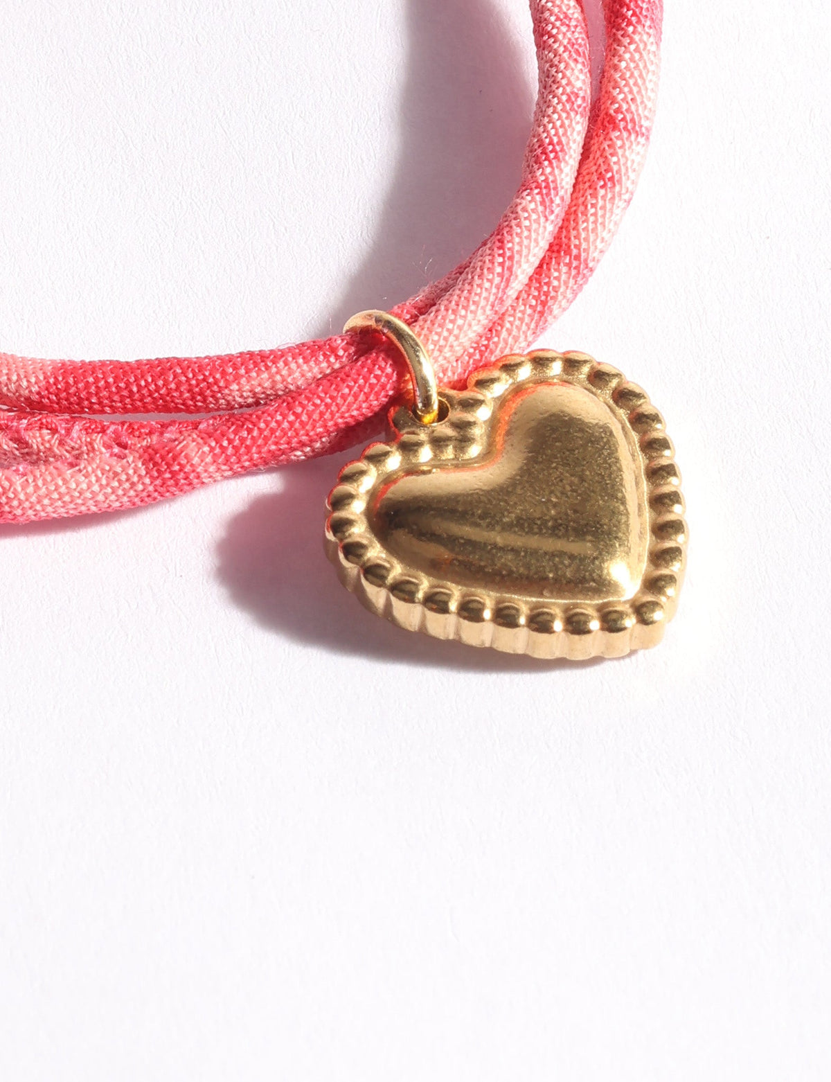 Pink abstract patterned cord bracelet with a gold-tone heart-shaped charm shown in close-up on white background