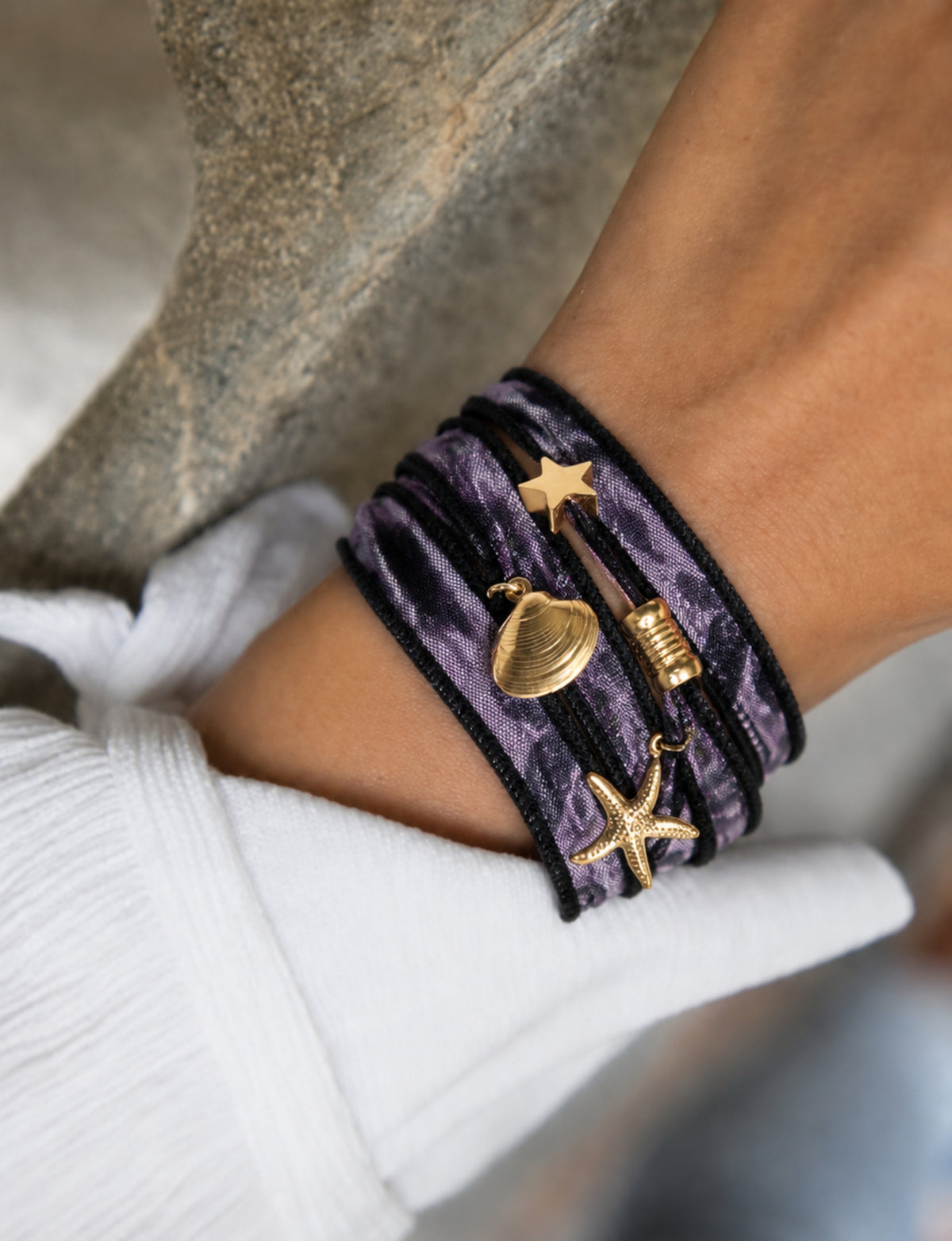 Purple wrap-around bracelet with black edges and gold star, shell, and starfish charms worn on wrist