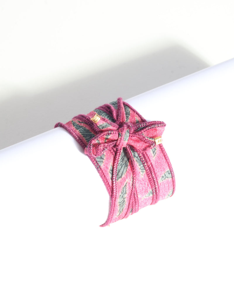 Pink and green abstract patterned fabric wrap-around bracelet with gold-tone charm, shown flat on white background