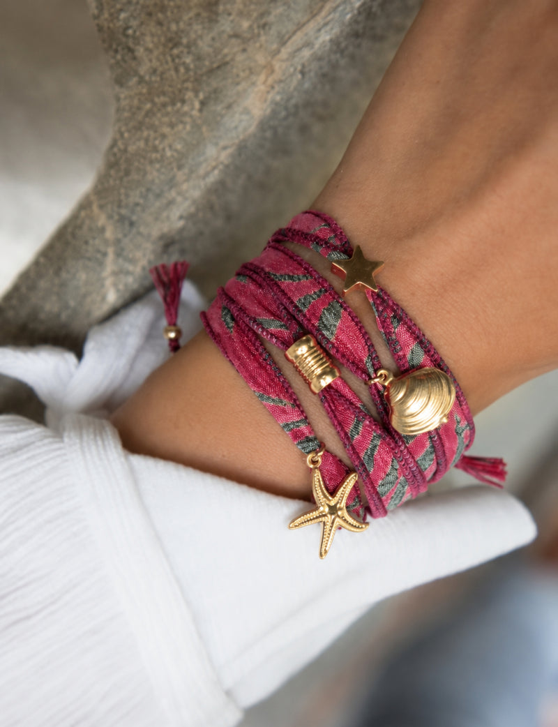 Wrap-around bracelet in pink fabric with green abstract pattern, gold star, shell, and starfish charms, worn on wrist