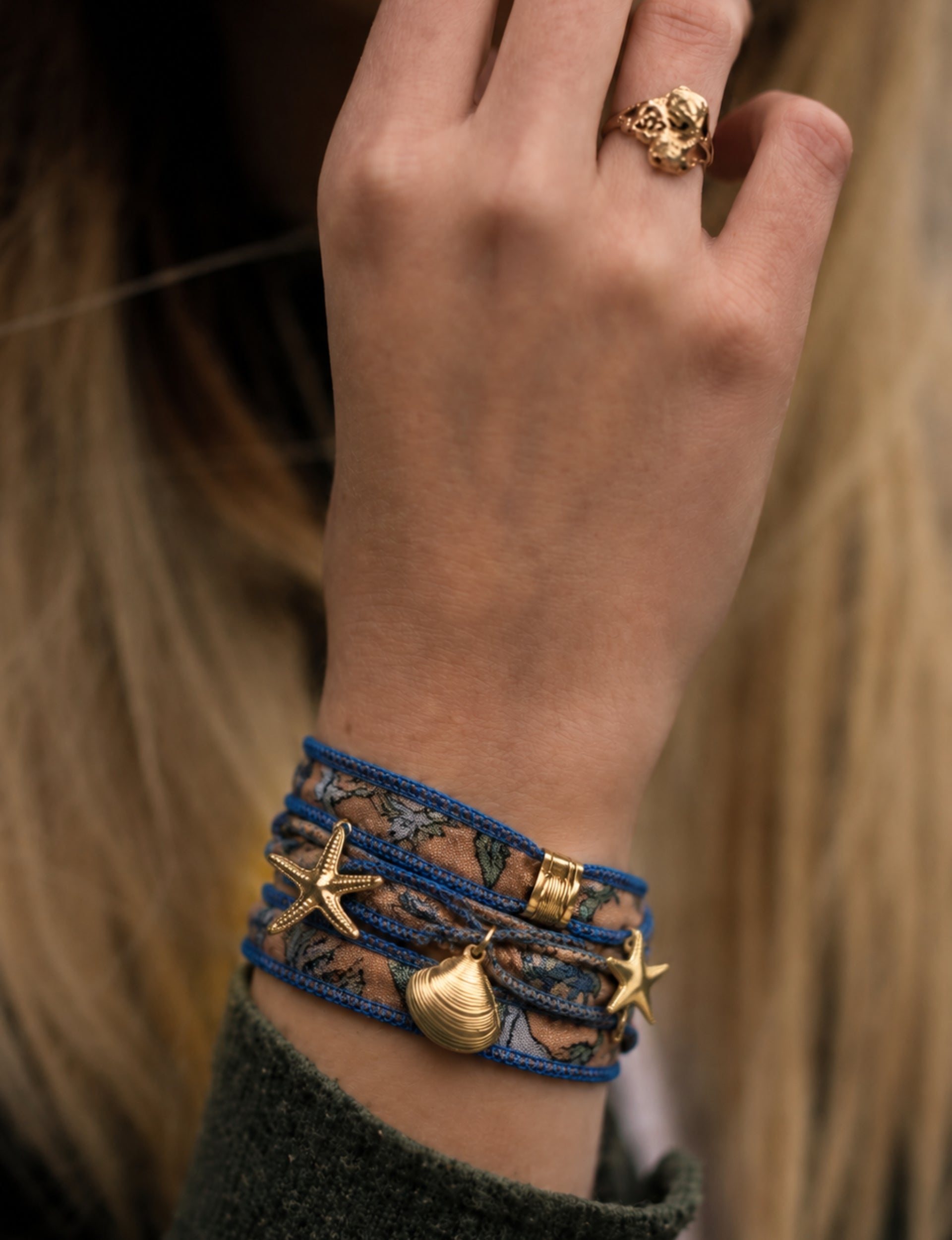 Blue wrap-around bracelet with floral fabric and gold starfish and shell charms worn on wrist with green sleeve