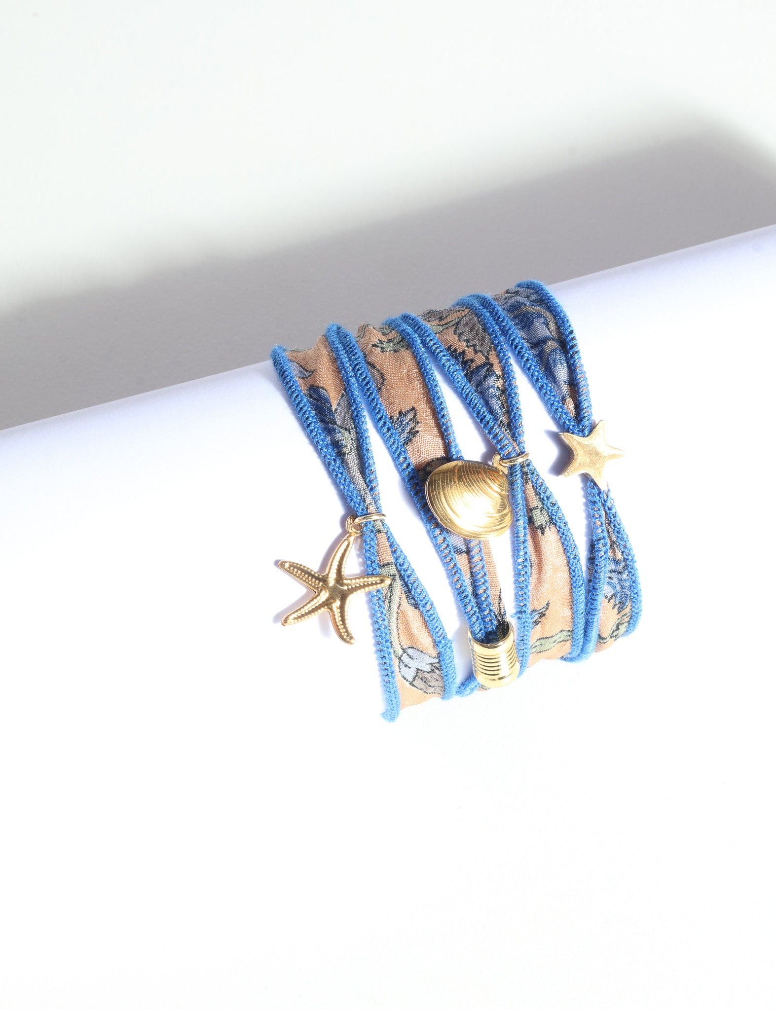 Wrap-around bracelet with blue-edged orange abstract fabric and gold-tone starfish, shell, and star charms on white background