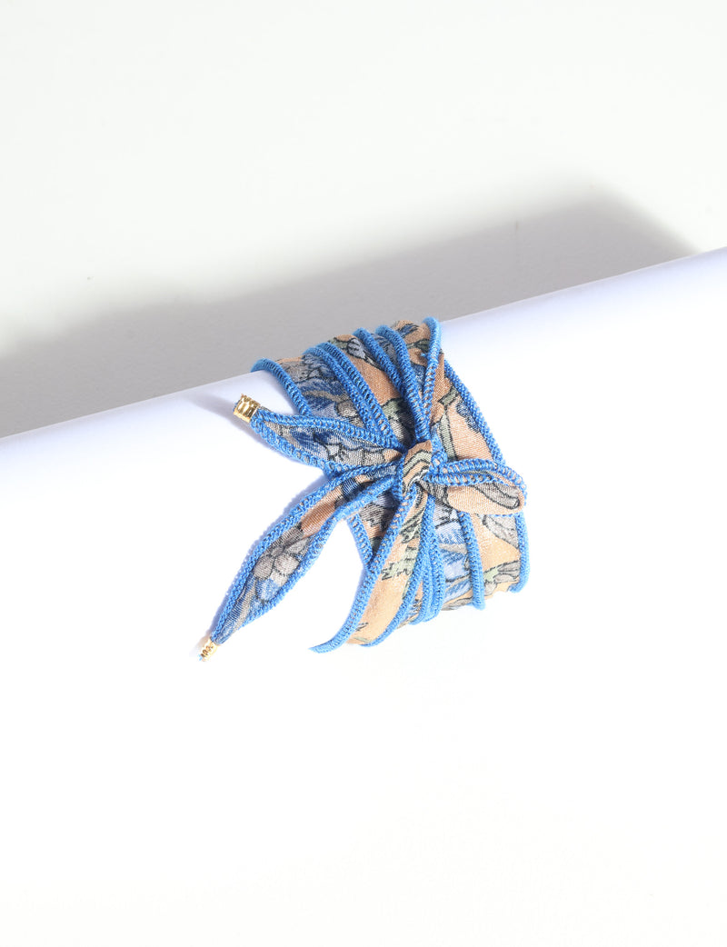 Wrap-around bracelet with blue-edged orange and blue abstract patterned fabric tied in a bow on white background