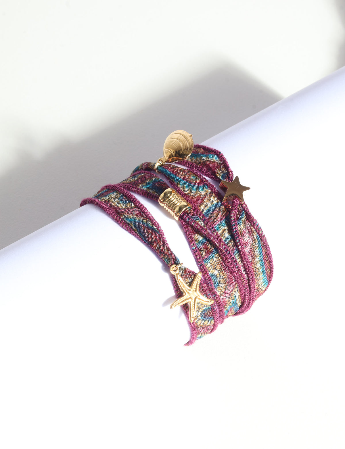Wrap-around bracelet with orange, blue, and gold abstract fabric and gold star, shell, and starfish charms, flat lay view