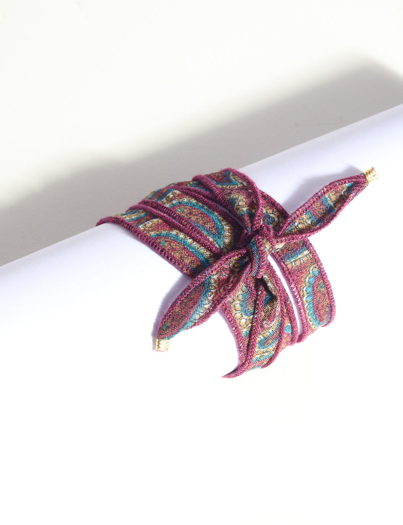 Wrap-around bracelet with orange, teal, and gold abstract pattern, burgundy edges, tied in a bow, flat on white surface