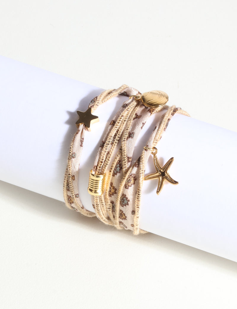 Wrap-around bracelet with beige fabric strap featuring abstract orange pattern and gold star, shell, and starfish charms