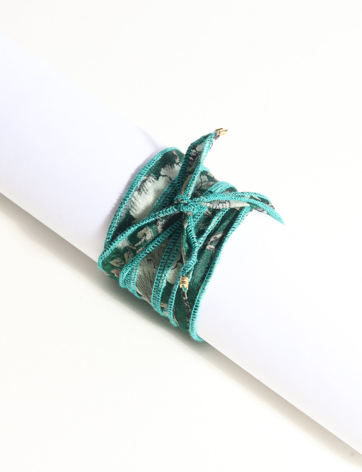 Green fabric wrap-around bracelet with abstract pattern and gold-tone charm tips, shown flat on white background