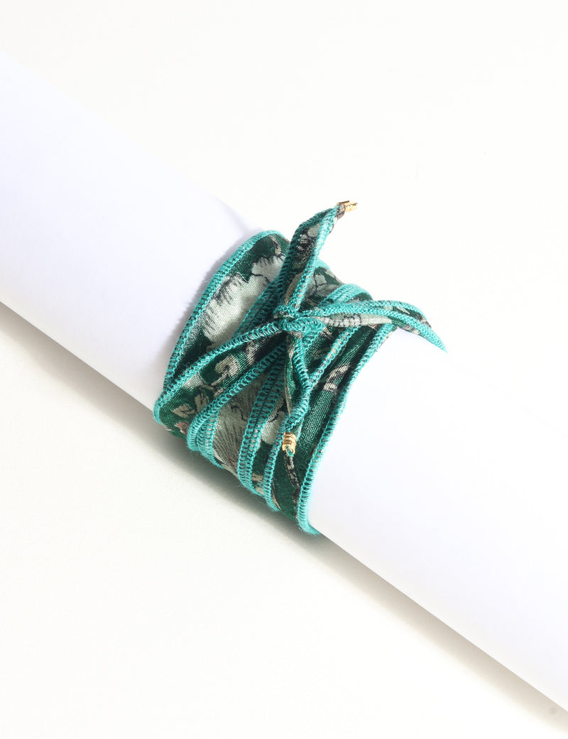 Green fabric wrap-around bracelet with abstract pattern and gold-tone charm tips, shown flat on white background
