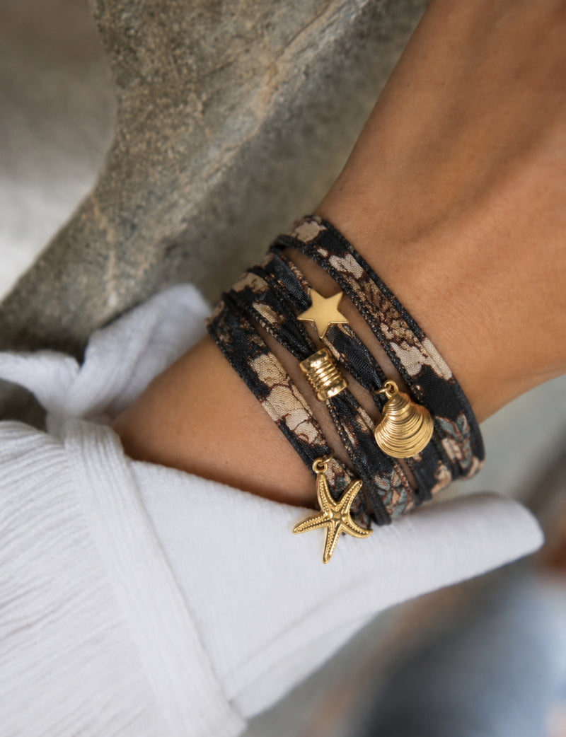 Wrap-around bracelet with orange and black abstract fabric and gold-tone star, shell, and starfish charms on wrist