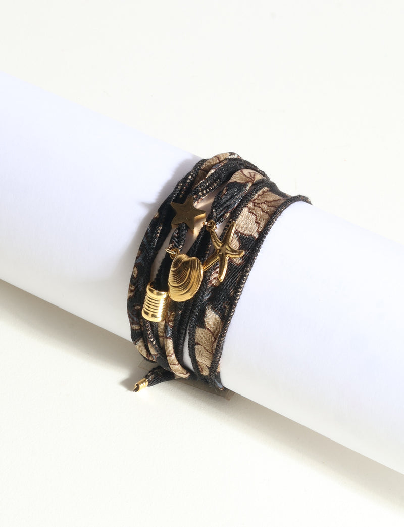 Wrap around bracelet in black and brown fabric with gold-tone star, shell, and starfish charms on white display