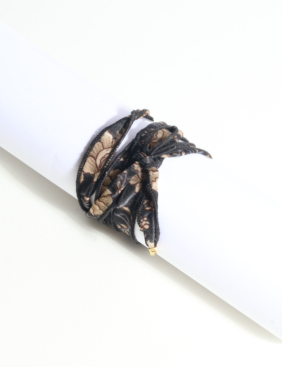 Black and beige floral fabric wrap-around bracelet with gold-tone charm, shown flat on white background