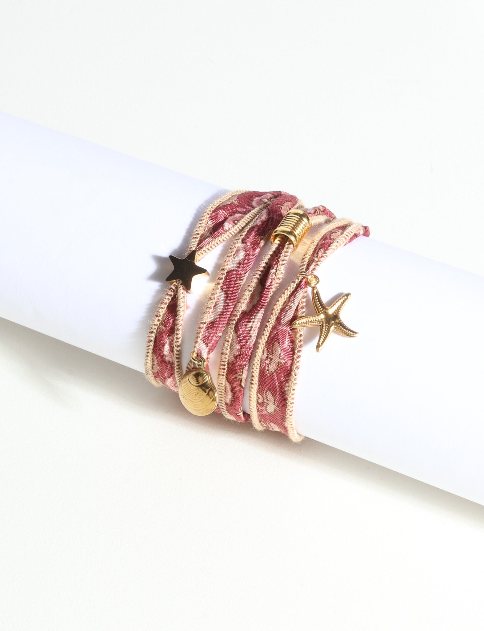 Wrap-around bracelet with orange abstract patterned fabric and gold-tone star, shell, and starfish charms on white display