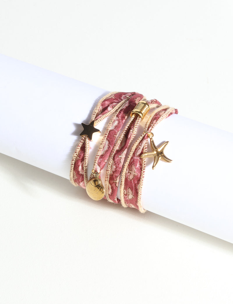 Wrap-around bracelet with orange abstract patterned fabric and gold-tone star, shell, and starfish charms on white display