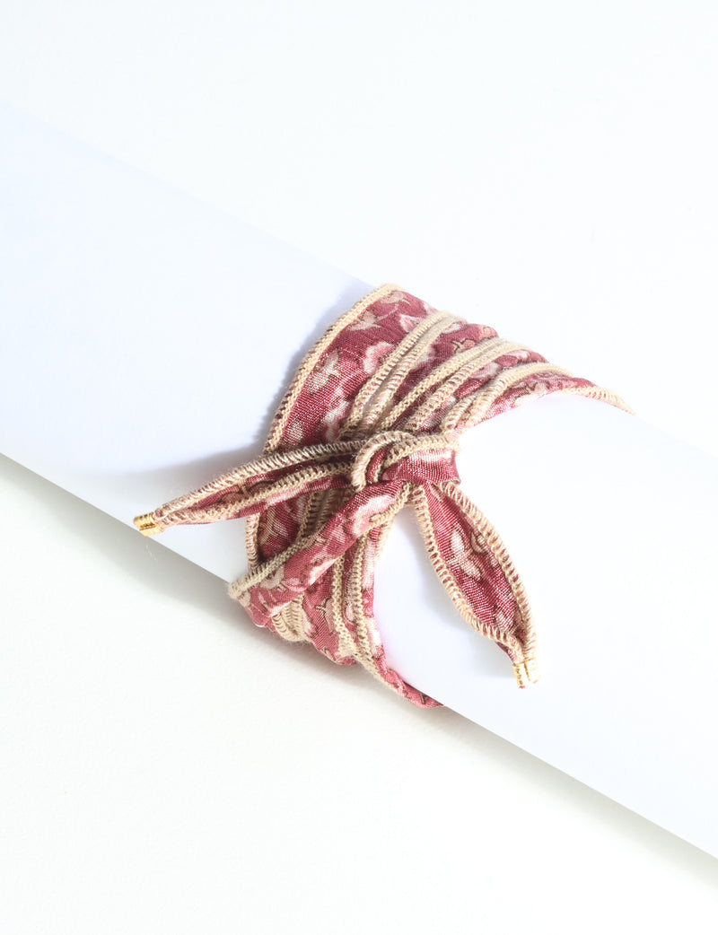 Wrap-around bracelet with orange abstract floral fabric and beige stitched edges, tied in a bow on white display