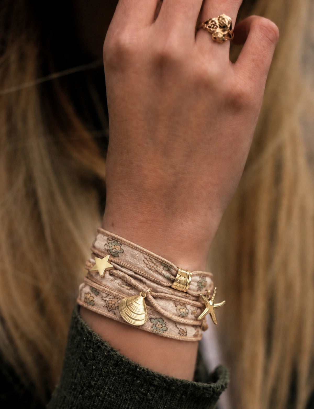 Beige wrap-around fabric bracelet with small floral print and gold-tone star, shell, and bird charms worn on wrist