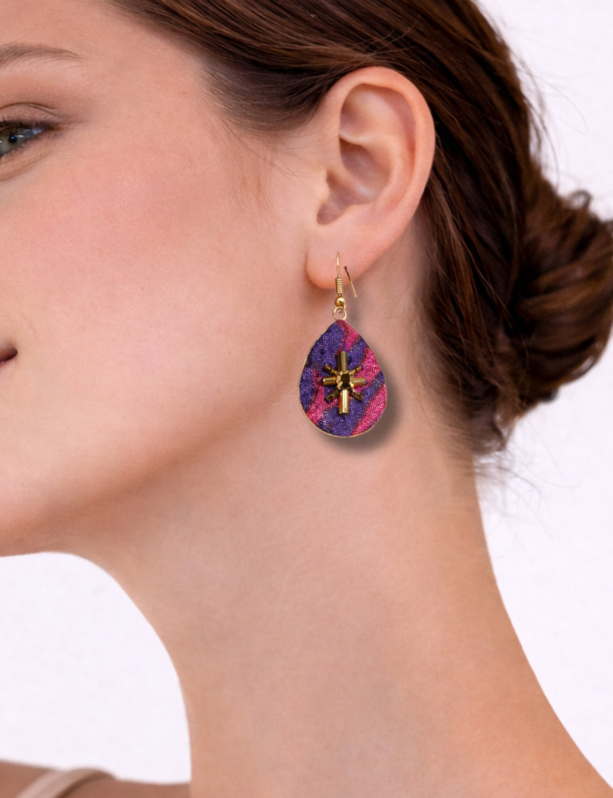Pink and purple abstract teardrop earrings with gold-tone bead embellishments worn on a woman's ear, side view