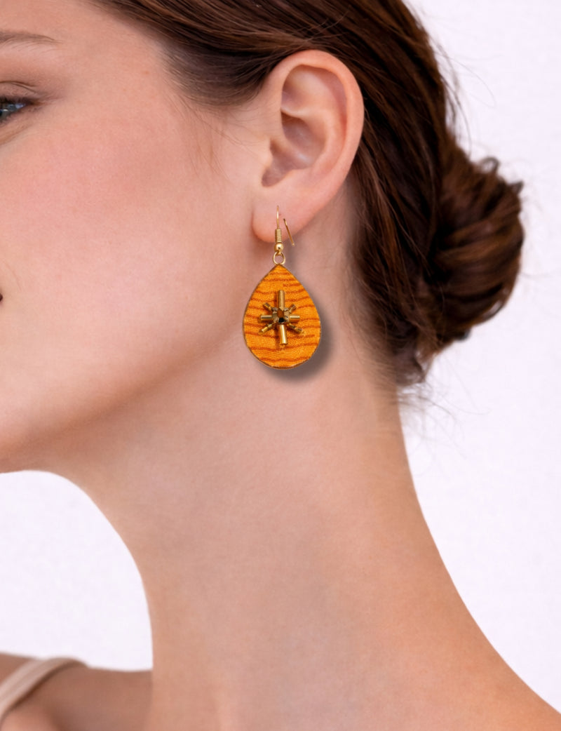 Yellow teardrop-shaped earrings with abstract gold bead design worn on a woman's ear, side profile view