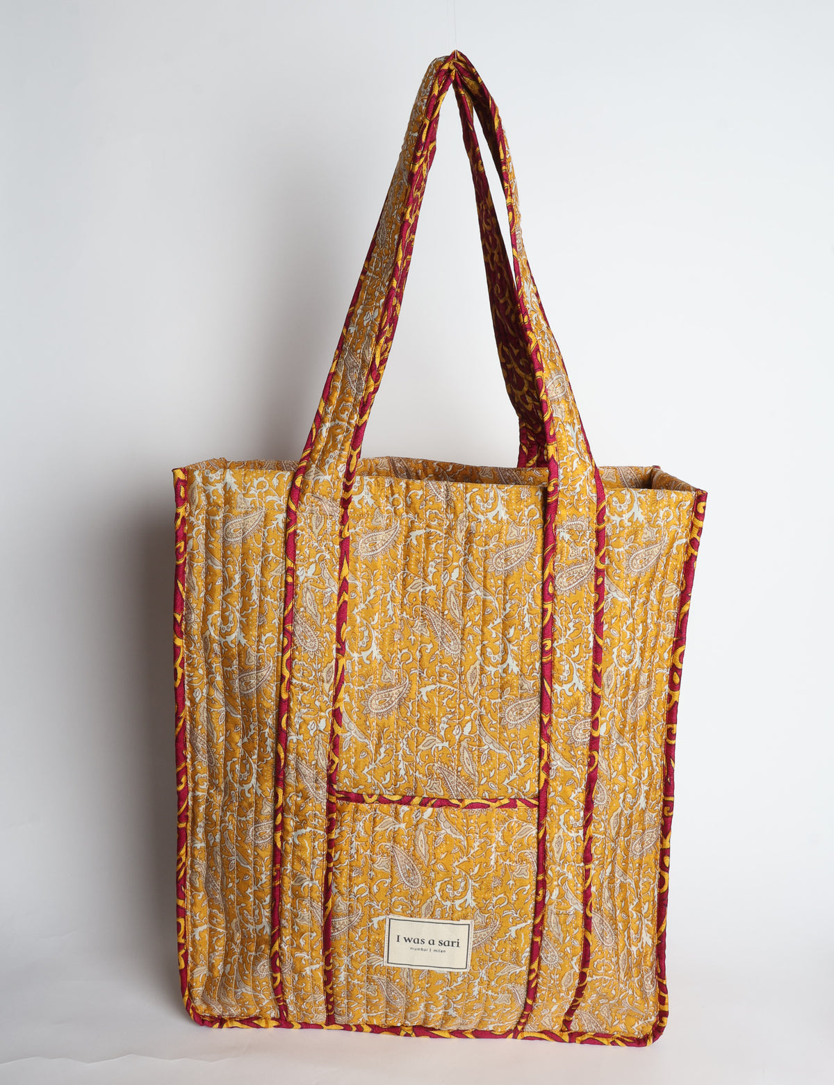 Quilted carry-all tote bag with a structured rectangular shape, long shoulder straps, and an external patch pocket.