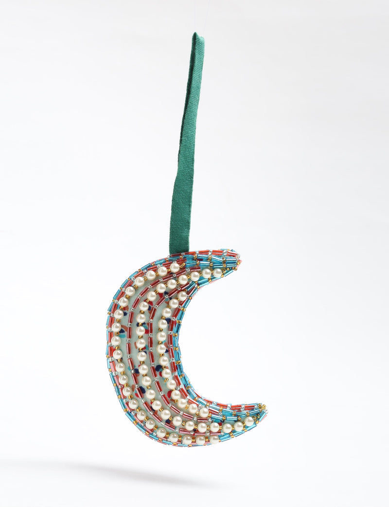 Crescent moon ornament decorated with pearl beads and red, blue, and gold cylindrical beads hanging by a green fabric loop