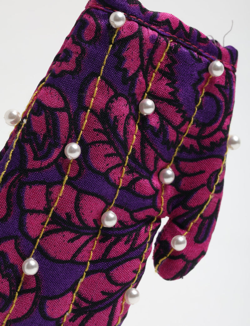 Close-up of purple and pink fabric mitten ornament with black floral pattern, yellow stitching, and white pearl bead accents