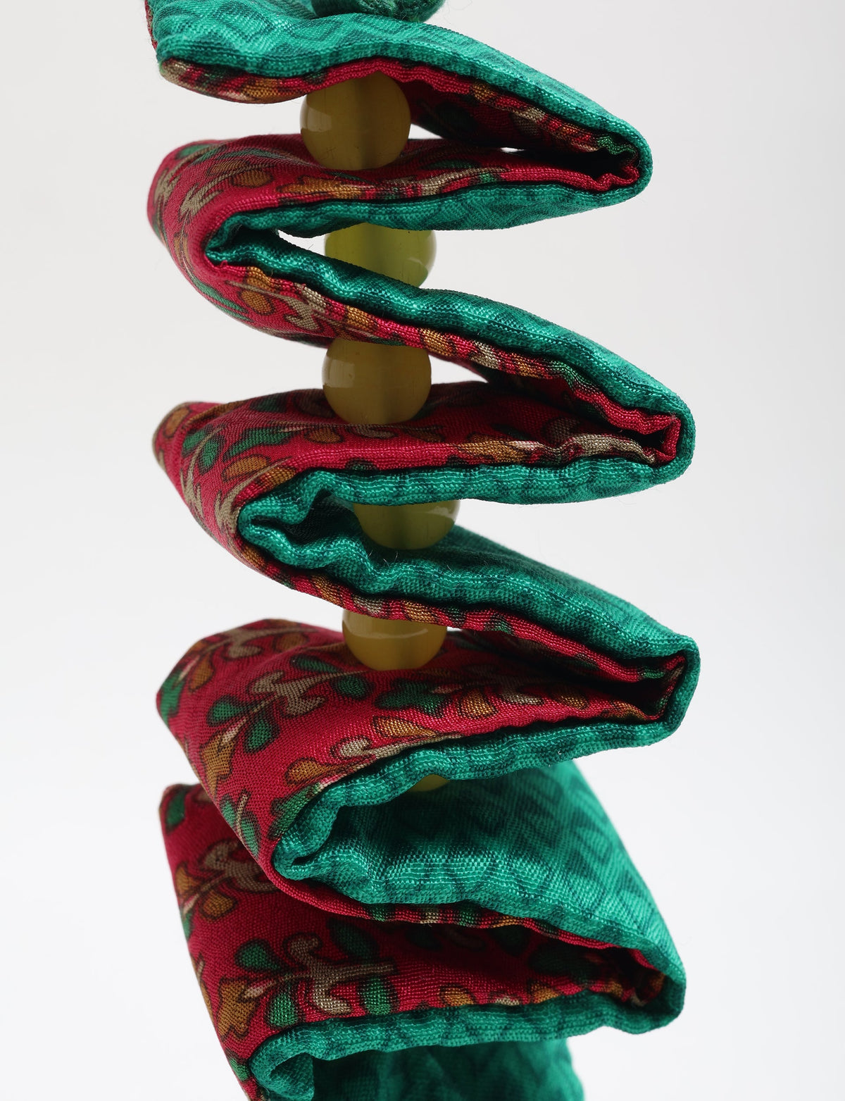 Close-up of a twisted fabric candy cane ornament with red and green patterned cloth and yellow beads threaded inside