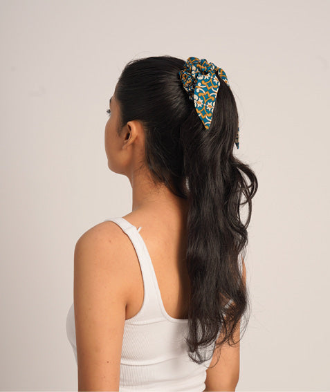 Woman wearing a teal and mustard abstract patterned fabric scrunchy with a bow, styled in a high ponytail, side back view