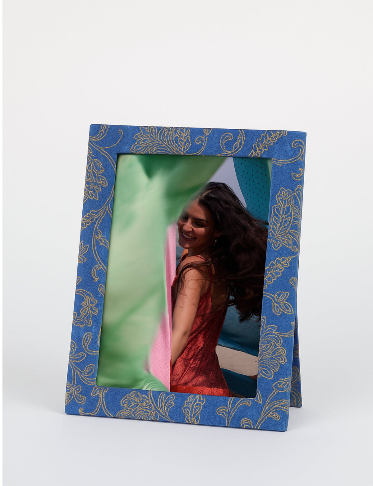 Blue photo frame with gold floral pattern, standing, holding a photo of a woman in a red dress with flowing hair outdoors
