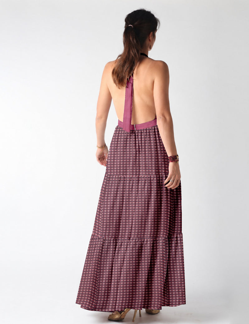 Woman wearing a backless maxi tiered dress with pink and dark leaf pattern and halter neck strap, shown from the back