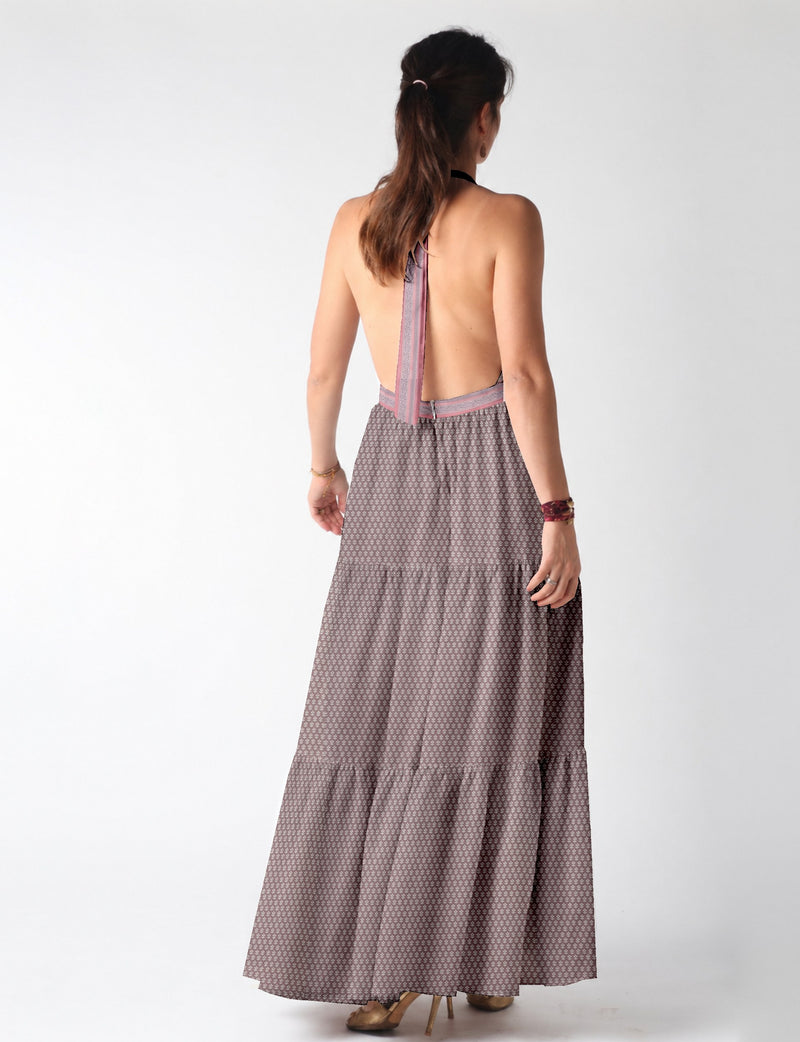 Woman wearing backless purple maxi tiered dress with micro pattern and halter neck tie, shown from back view