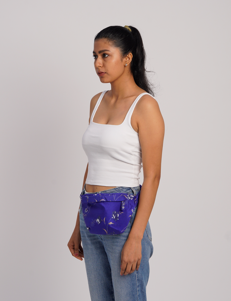 Woman wearing a blue midi belt bag with a floral micro design, paired with light blue jeans and a white tank top, side view