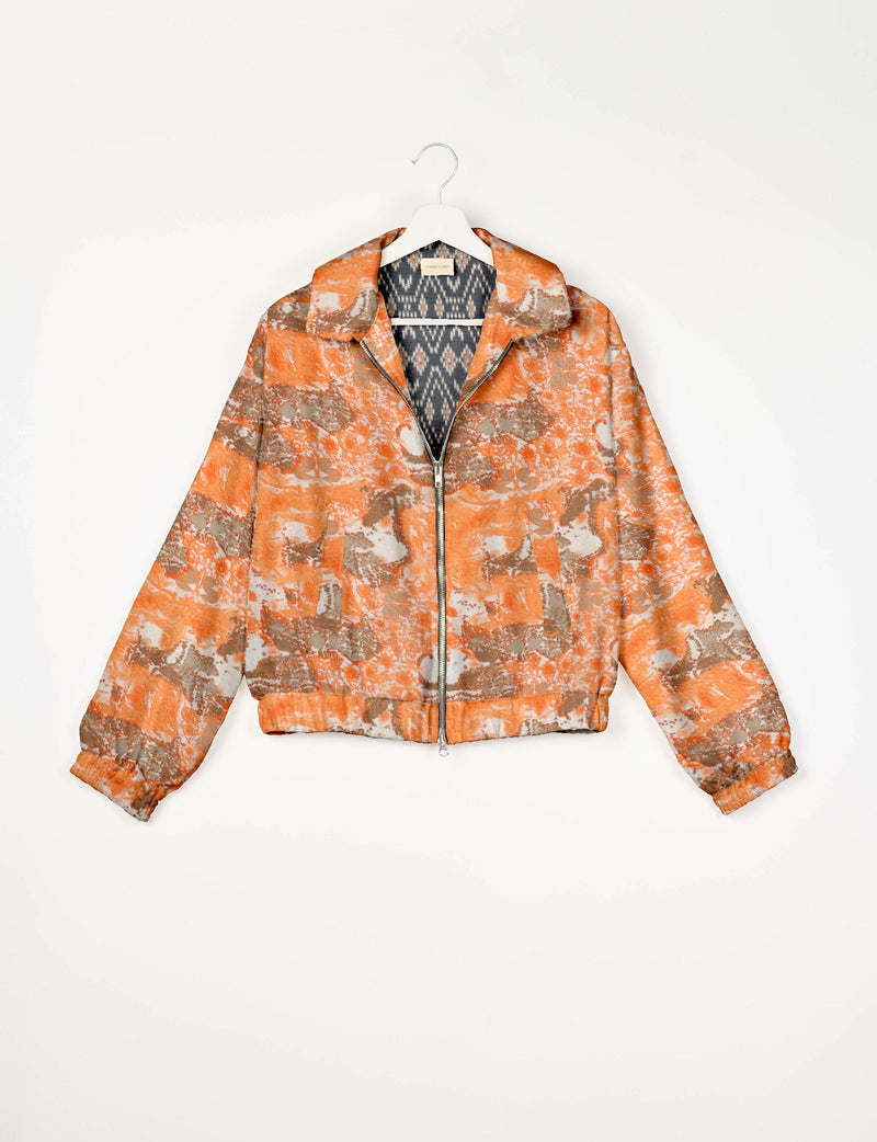 Orange abstract patterned bomber jacket with front zipper and elastic cuffs, shown hanging on a white hanger