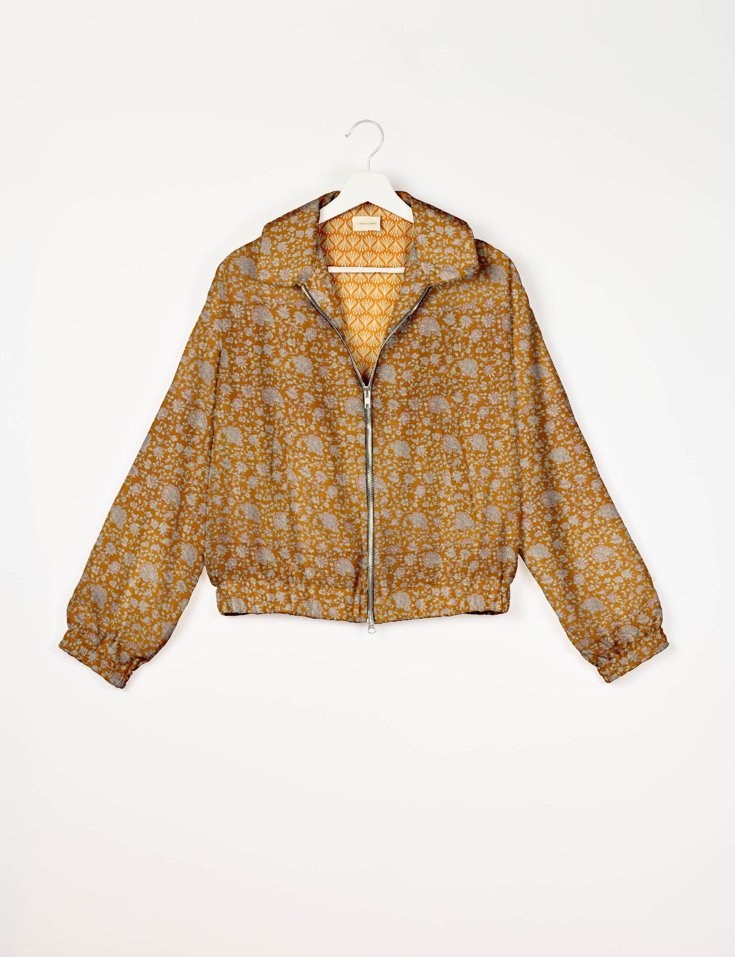 Orange floral bomber jacket with front zipper, elastic cuffs and hem, hanging on white hanger, front view