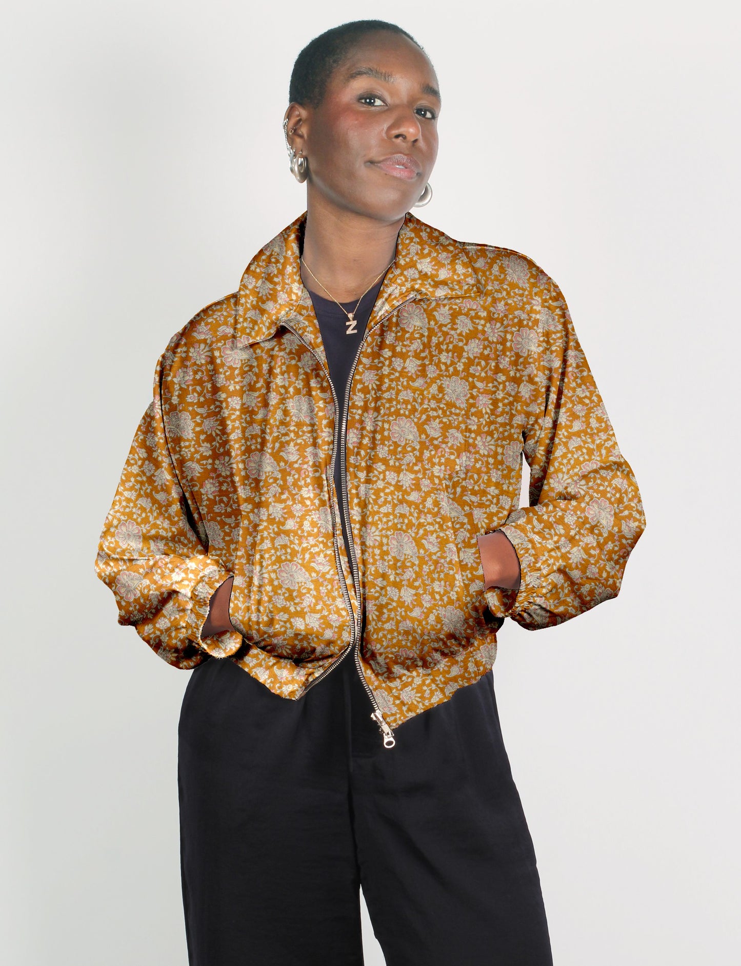 Woman wearing an orange floral bomber jacket with a front zipper and elastic cuffs, paired with black pants