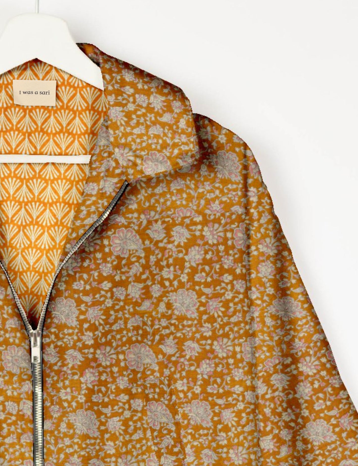 Orange floral patterned bomber jacket with silver zipper, shown on hanger with label reading "I was a sari" and patterned