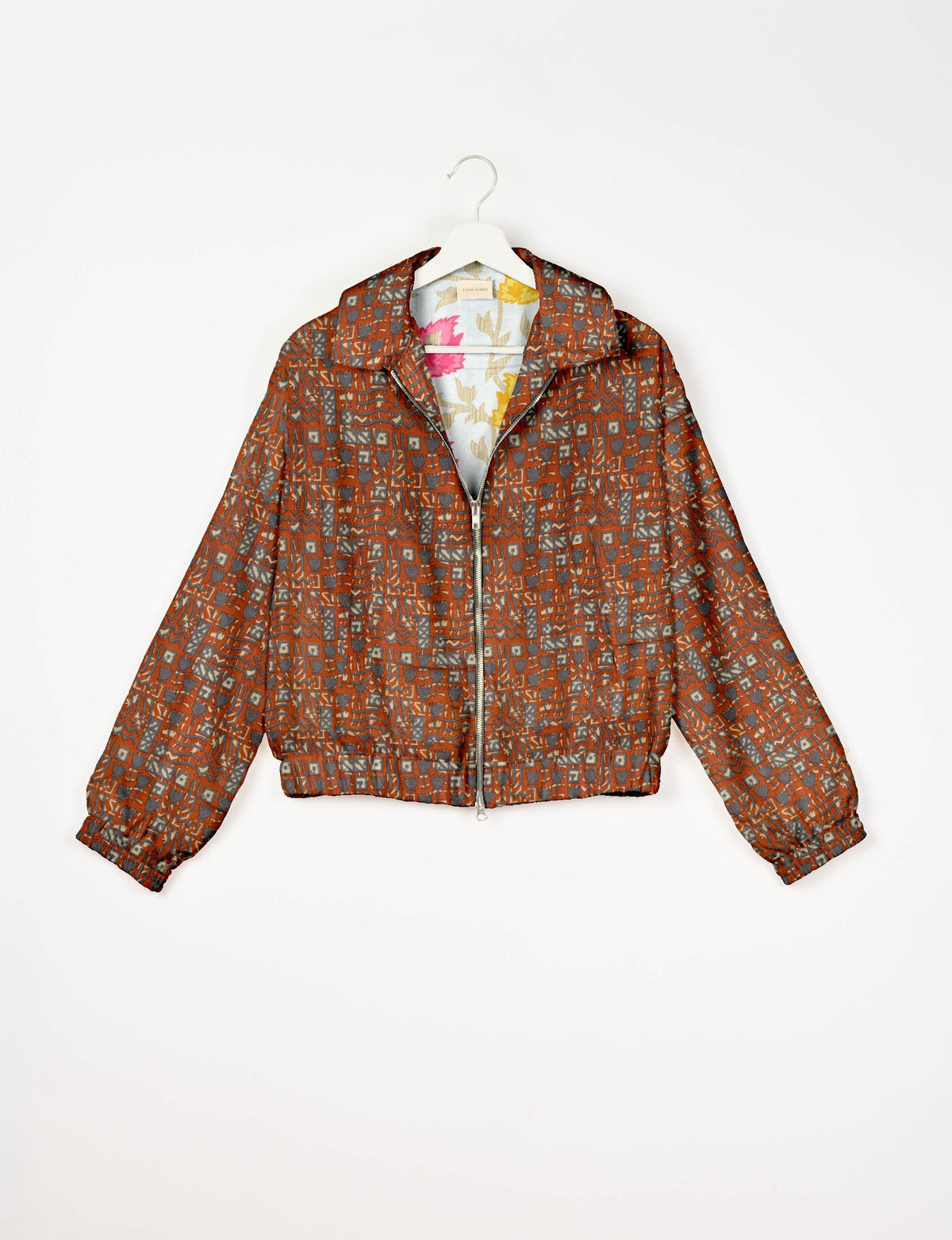 Orange bomber jacket with Indian ethnic geometric pattern, front zipper, collar, and elastic cuffs, shown on hanger front
