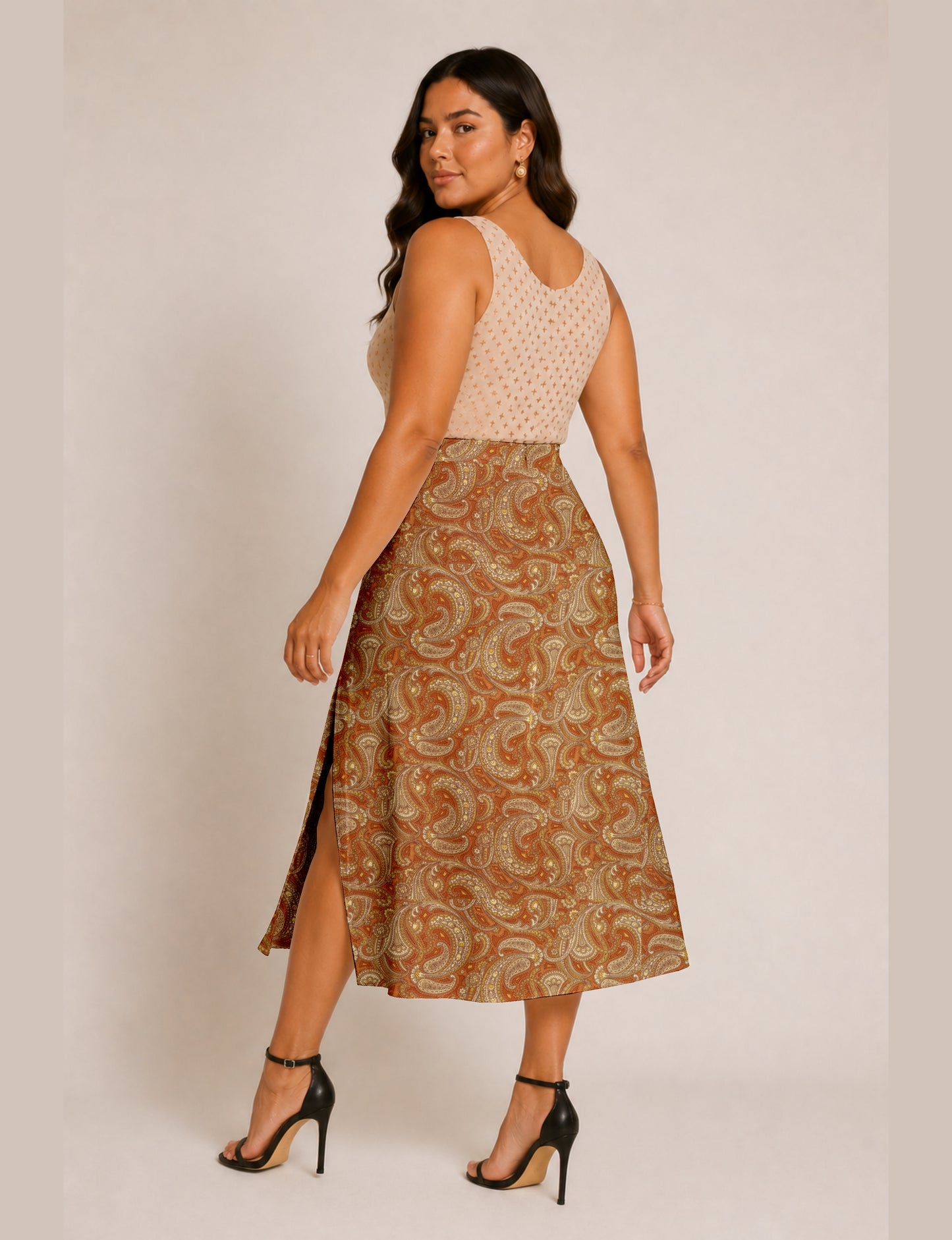 Woman wearing an orange paisley A-line skirt with side slit, paired with a sleeveless beige top with small cross patterns