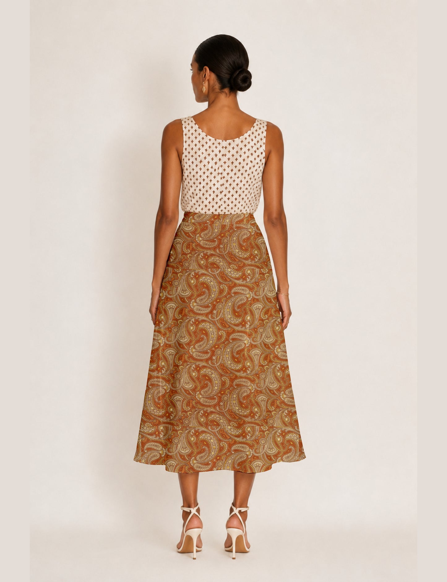 Woman wearing orange paisley A-line skirt with slit, paired with sleeveless white top with brown cross pattern, back view