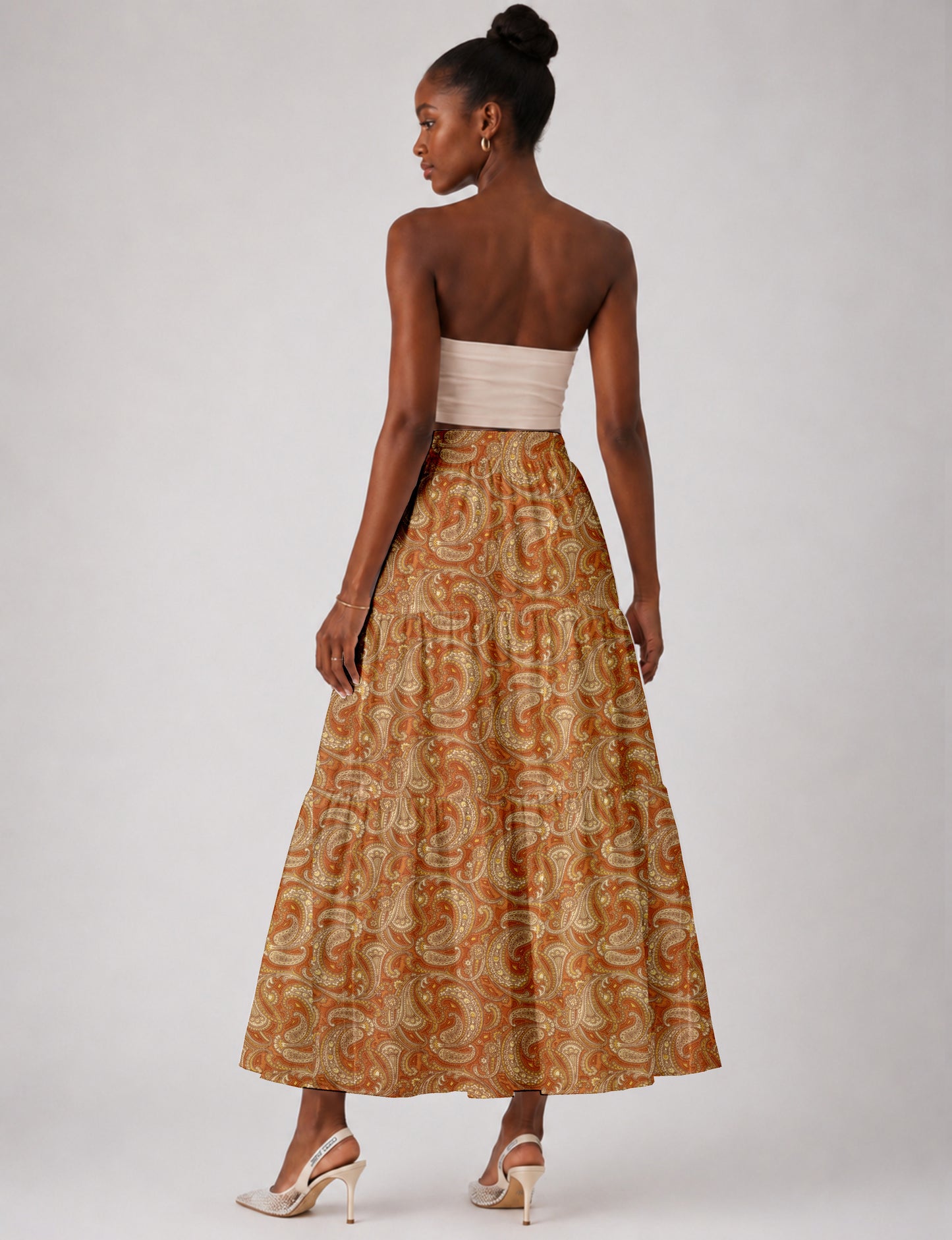 Woman wearing an orange paisley midi tiered skirt with a high waist, shown from the back in a studio setting