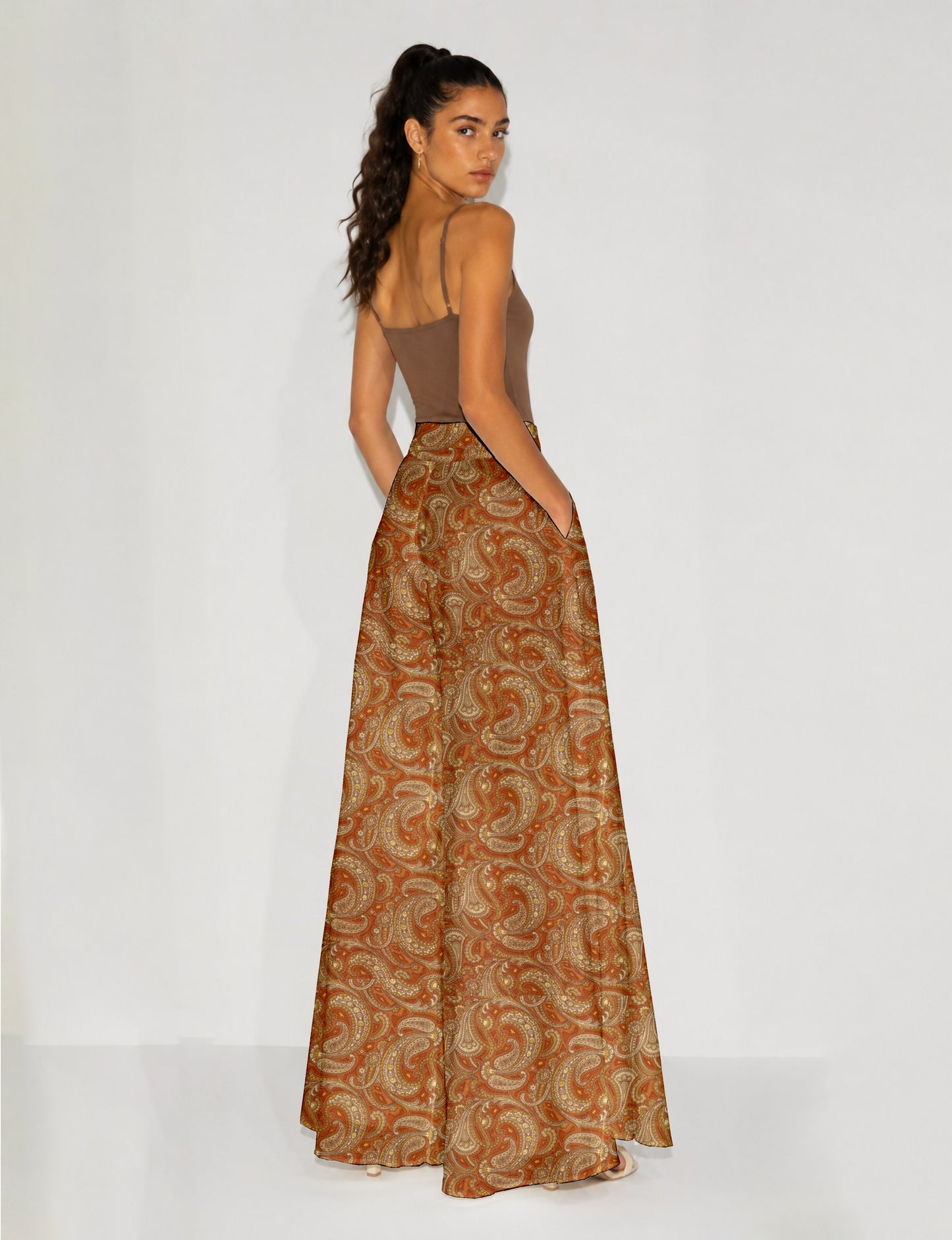 Woman wearing wide leg palazzo trousers with orange paisley pattern, side pockets, shown from back, paired with brown tank