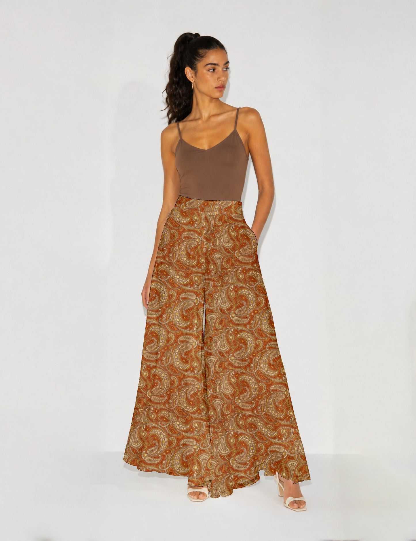 Woman wearing wide leg palazzo trousers with orange paisley pattern, paired with brown sleeveless top and white heels