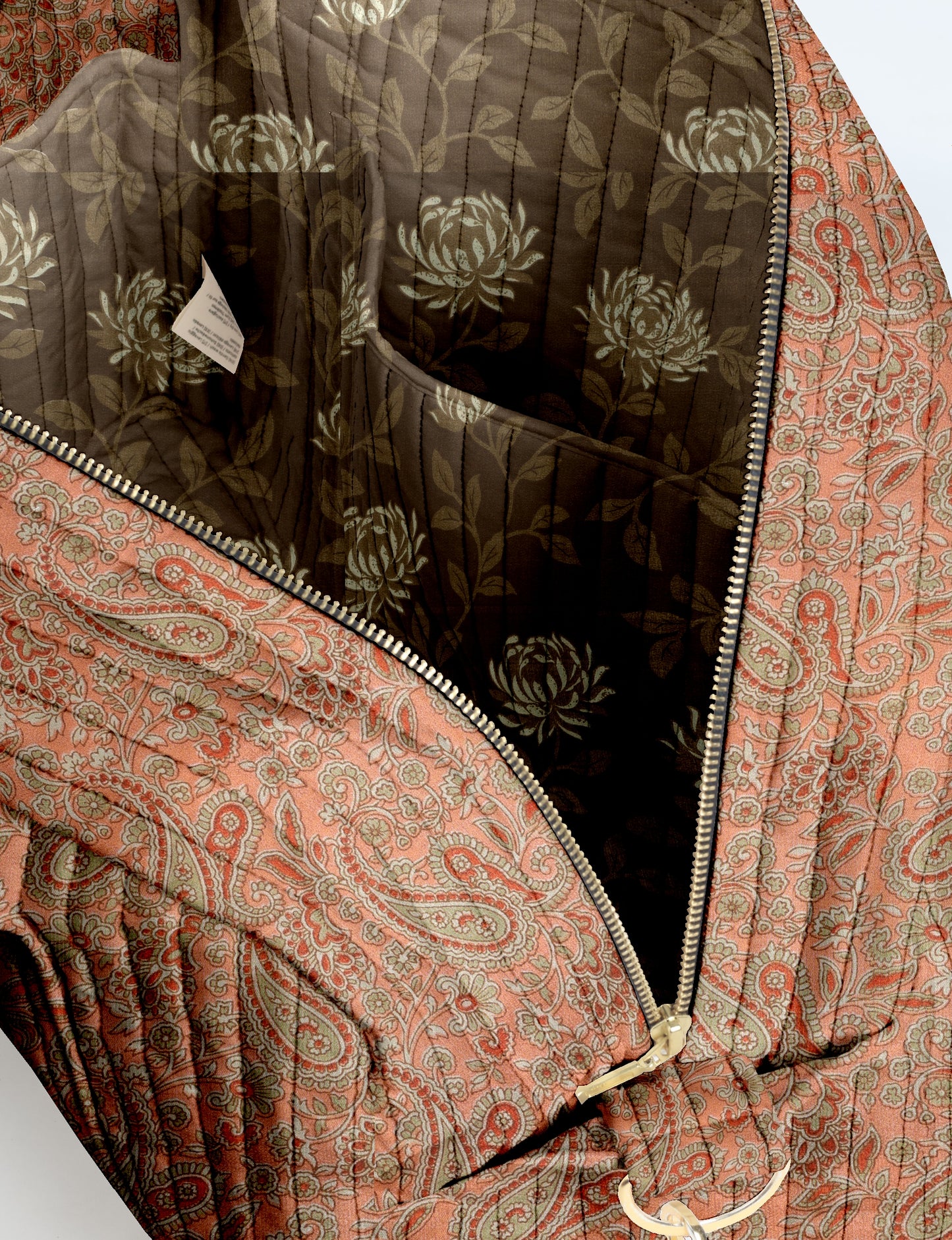 Quilted duffle bag with orange paisley exterior, zipper closure, and dark floral patterned interior lining with pocket