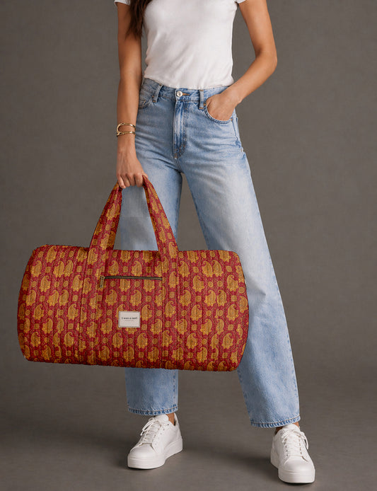 Quilted brown paisley barrel bag with double handles, front pocket, and gold zipper, shown in side angle view