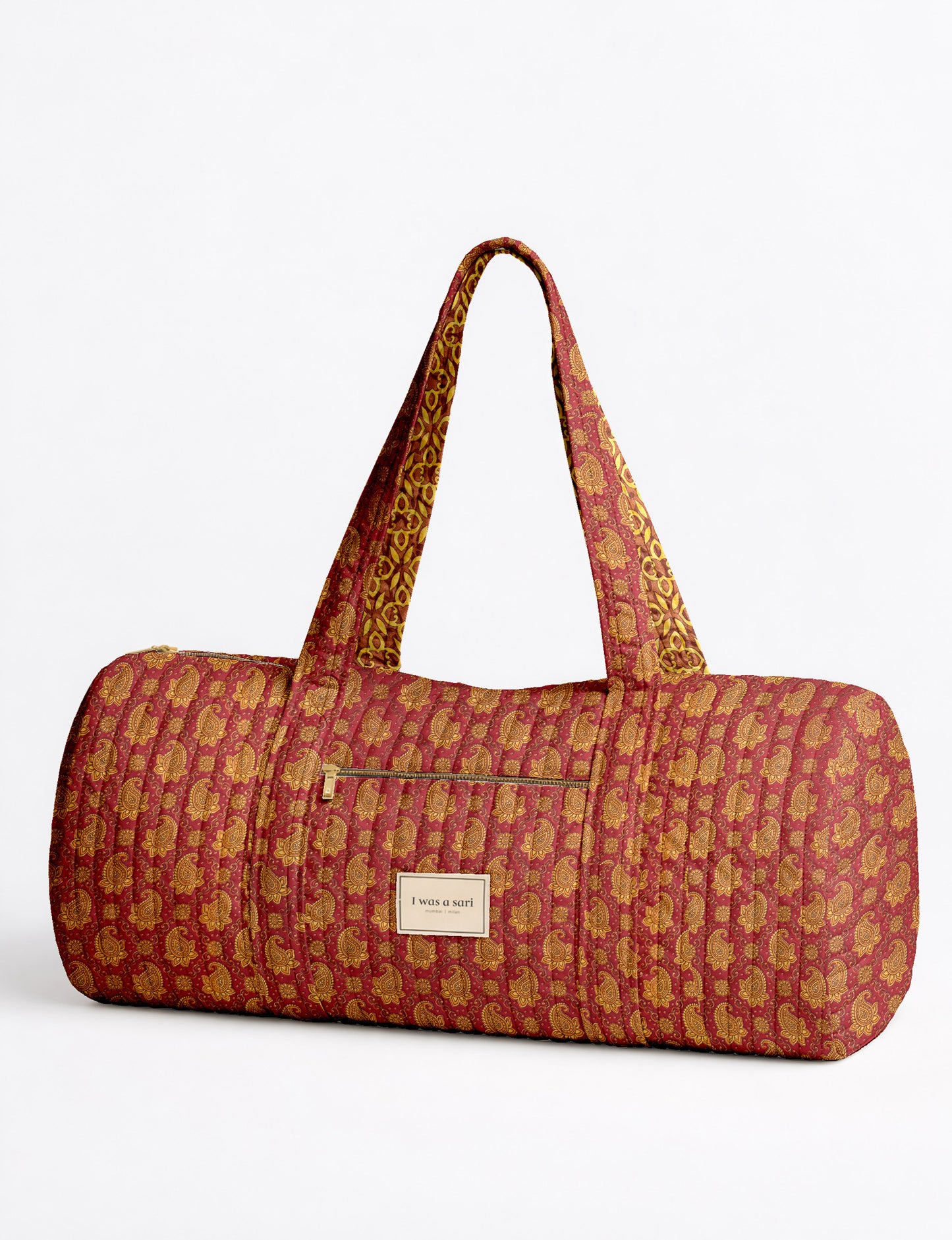 Brown paisley quilted bowling bag with front zipper pocket, held by person wearing white shirt and light blue jeans