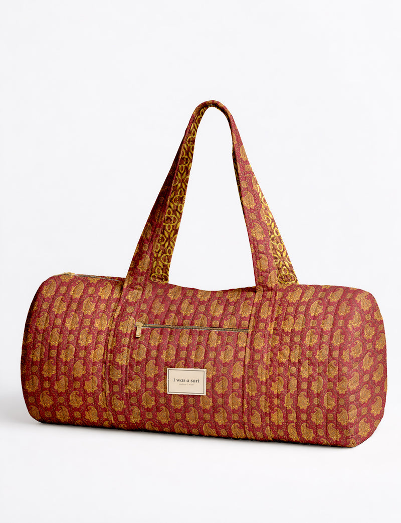 Brown paisley quilted bowling bag with front zipper pocket, held by person wearing white shirt and light blue jeans
