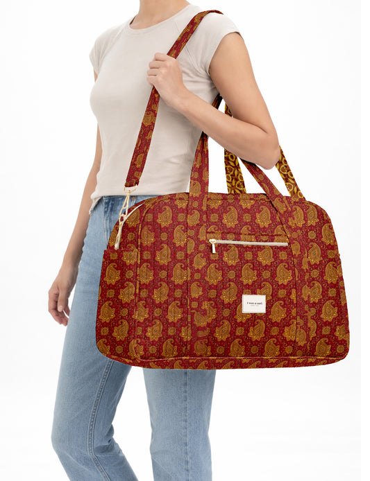 Brown quilted duffle bag with paisley pattern, front zip pocket, dual handles, and label reading "I was a sari"