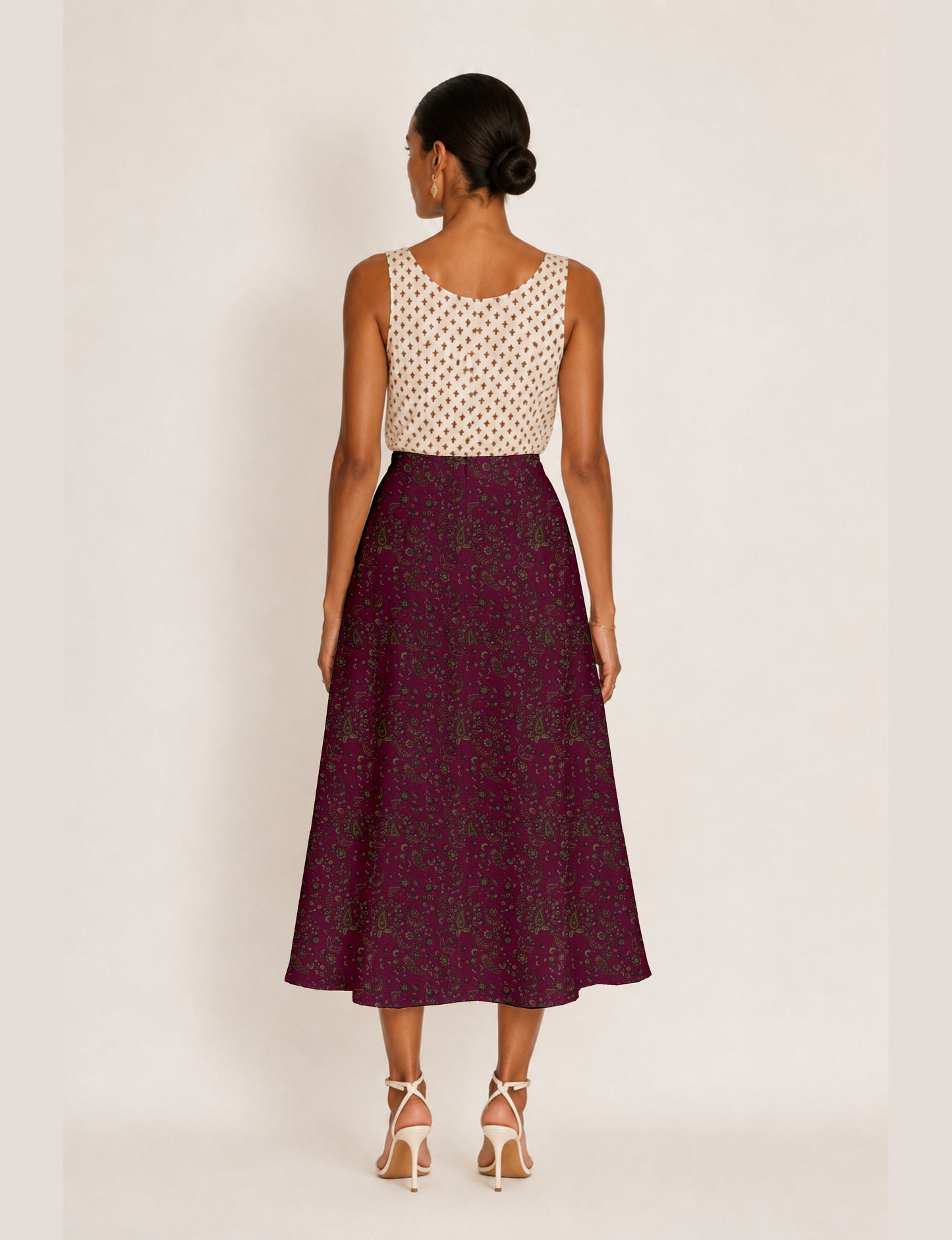 Woman wearing a yellow micro design A-line skirt with side slit, paired with a sleeveless beige top with small cross