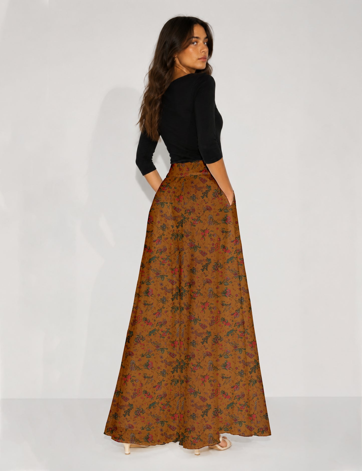 Woman wearing blue wide leg palazzo trousers with black and brown tropical floral print, side pockets, shown from back angle