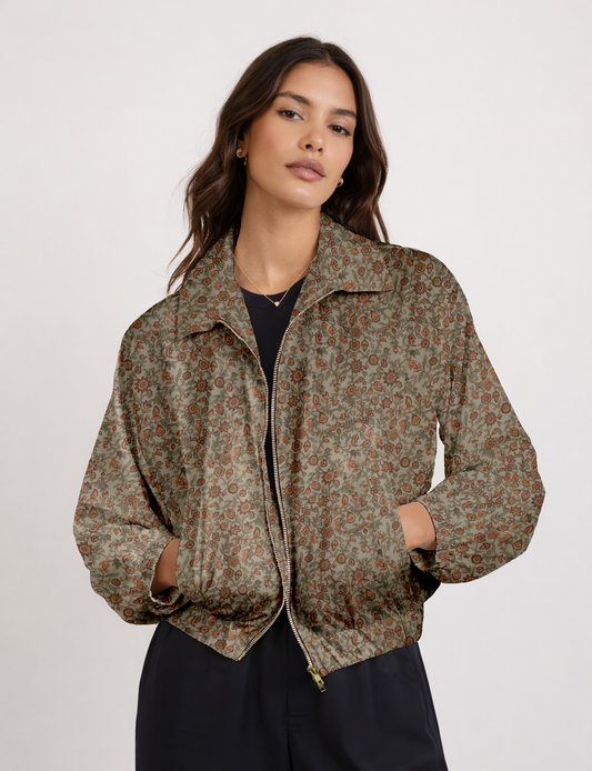 Woman wearing a zip-up bomber jacket with a green base and orange floral pattern, front view with hands in pockets